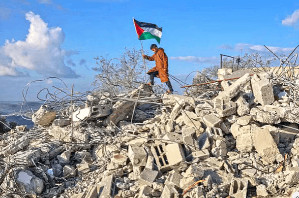 পশ্চিম তীরের ফিলিস্তিনি গ্রাম বাজরিয়ায় ইসরায়েলি সেনাবাহিনীর ধ্বংস করে দেওয়া একটি বাড়ির ধ্বংসস্তূপের ওপর পতাকা হাতে এক কিশোরএএফপি